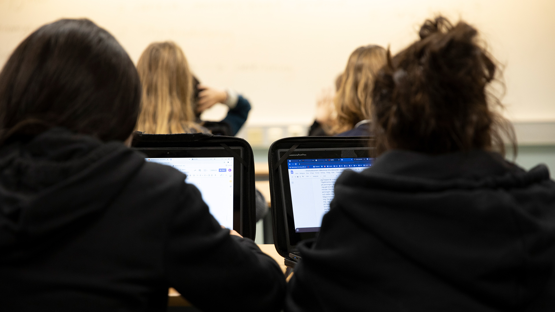 På bilden syns ryggtavlorna på två elever som arbetar på sina datorer.