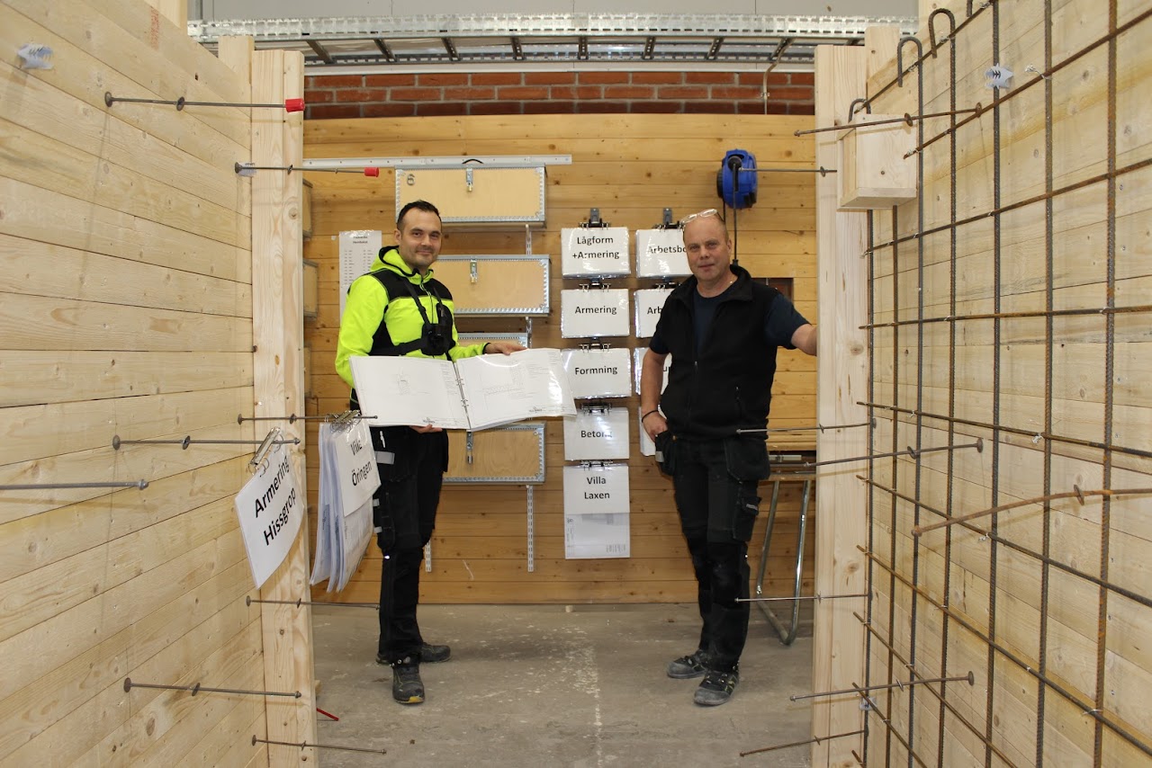 Bilden visar Petter Hjertén och Björn Falkenby som står i en bygg hall med uppsatta trä väggar, på väggarna sitter olika typer av armeringsjärn. 