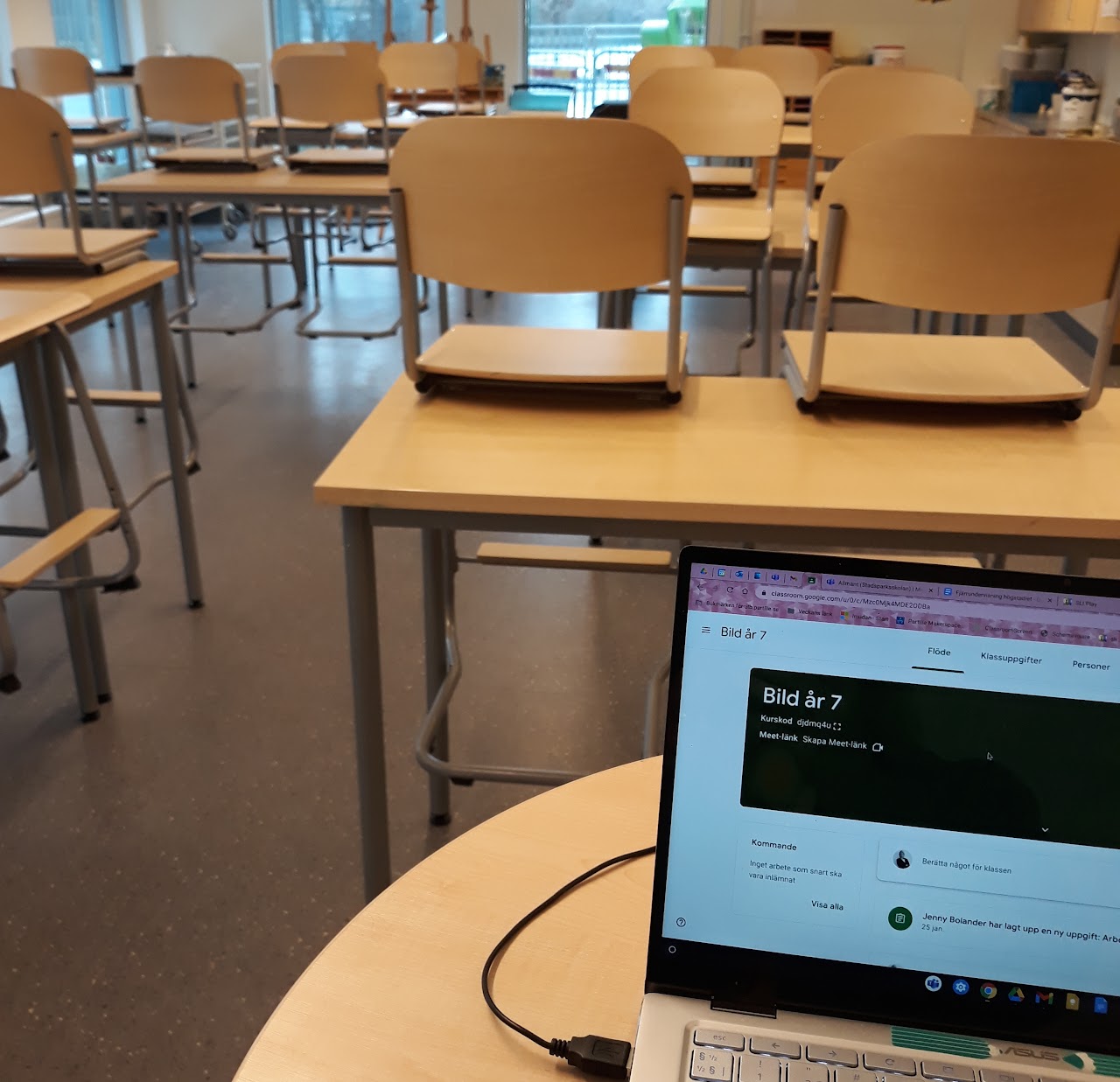 Bilden visar en uppslagen bärbar dator som står på en skolbänk, i bakgrunden finns fler bänkar med uppvända stolar på. 