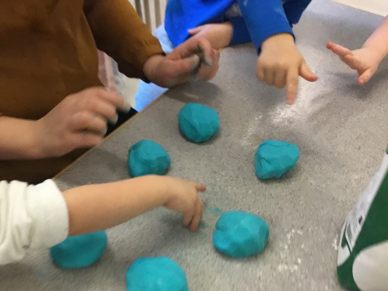 Bilden visar tre par barnhänder och på ett bord framför dem ligger sex stycken turkosa lerklumpar.