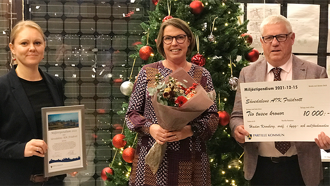 Bild på tre personer framför en julgran med röda kulor. 
