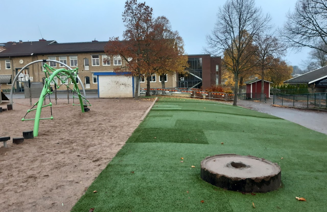 Bilden visar en skolgård där det på ena sidan är en sandlåda med en klätterställning i och på andra sidan är nylagt konstgräs. 