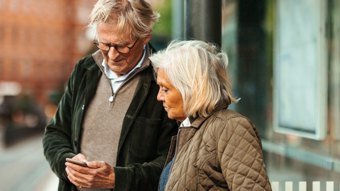 Bilden visar två personer som står utomhus. Den ena personen håller i en mobiltelefon som båda tittar på.