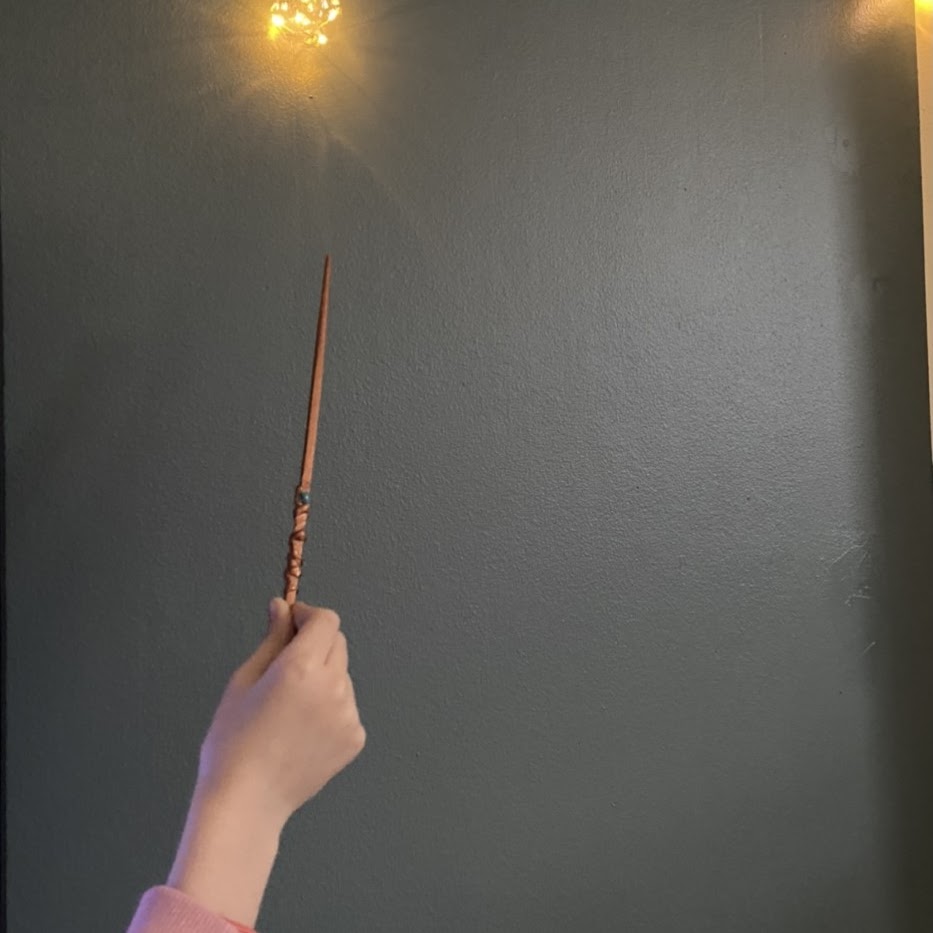 Bilden visar en hand som håller i ett trollspö, ovanför trollspöet lyser en lampa. 