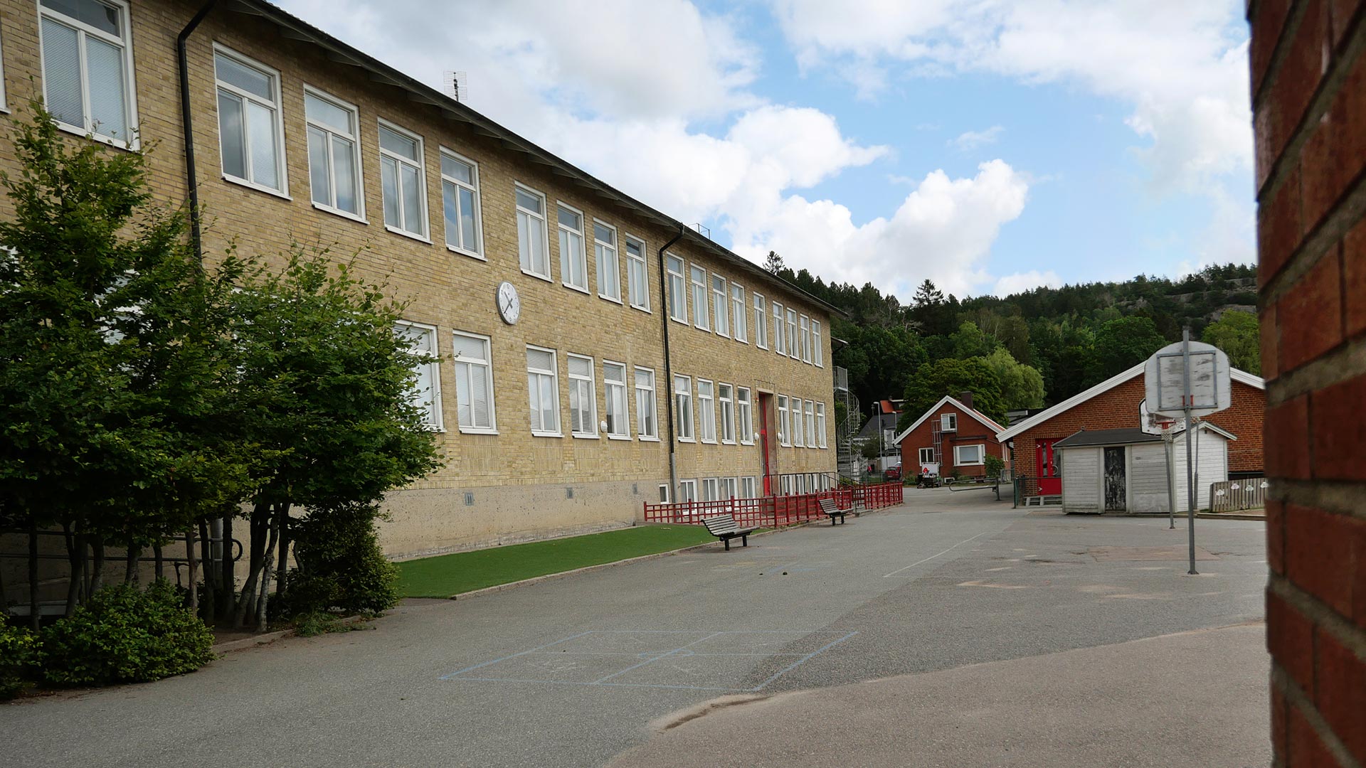Till vänster på bilden syns en tvåvåningsbyggnad i gult tegel och till höger om den ligger en enplansbyggnad i rött tegel. Mellan och framför dessa ligger skolgården med bland annat en basketkorg.  