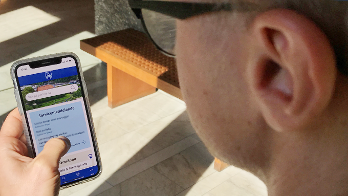 Man som håller mobiltelefon i handen som visar Partille kommuns webbplats i mobilt läge.