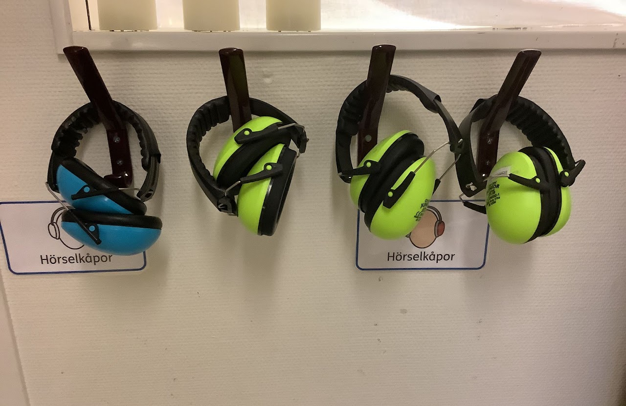 Bilden visar färgglada hörselkåpor som hänger på krokar på en vägg. 