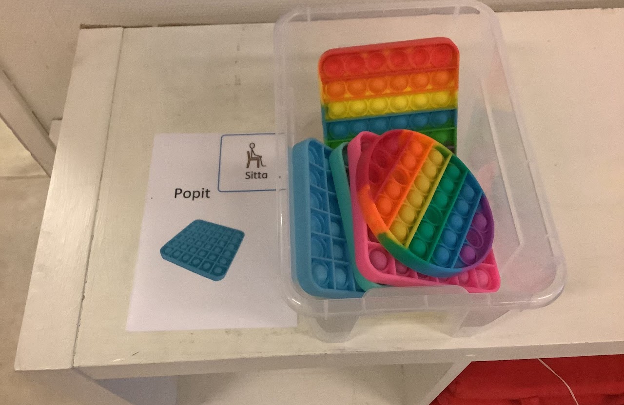 Bilden visar en låda med popit-plattor och ett bild-stöd som visar sitta och en popit-platta.
