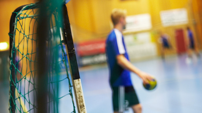 Bild tagen genom ett handbollsmål med en spelare i oskärpa. 