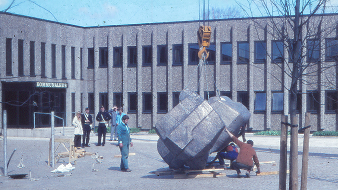 Bild på tre män som monterar fontänen valen utanför Partille kommunhus år 1971. Fem personer står vid sidan och tittar på. 