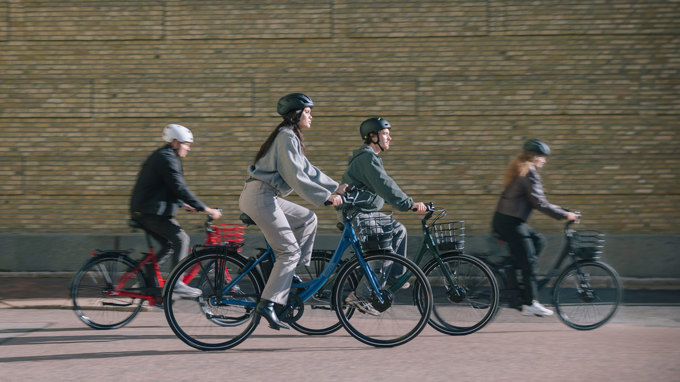Fyra personer med hjälm cyklar på varsin elcykel i stadsmiljö.