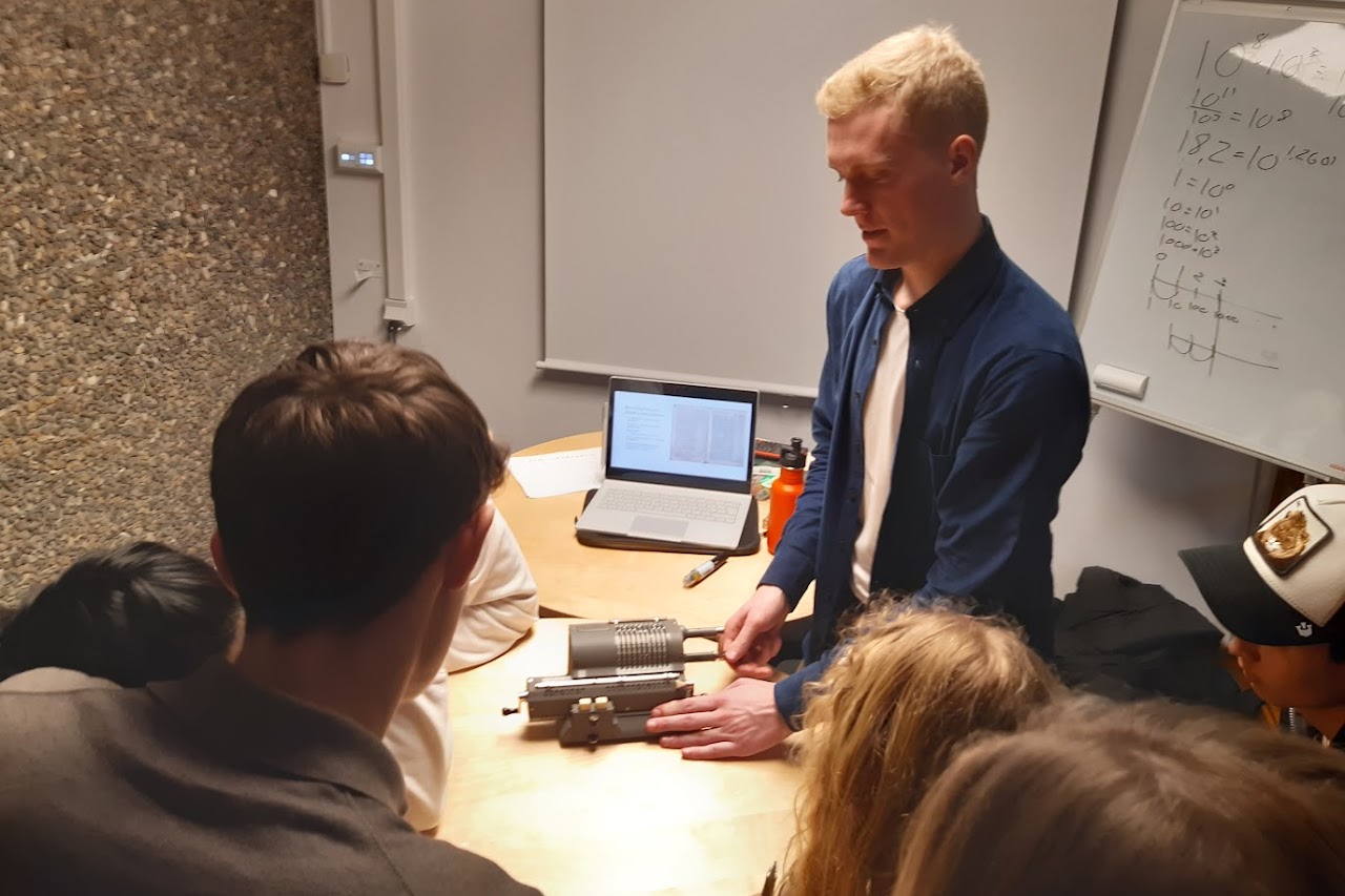 Bilden visar Nils Grimbeck som demonstrerar en räknesnurra på ett bord framme vid en vit tavla för flera nyfikna elever. 
