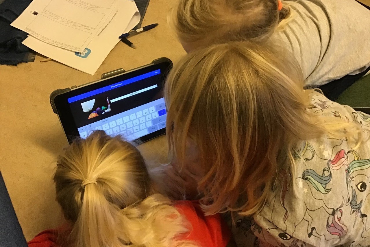 Bilden visar tre barn som sitter tätt ihop och tittar på en läsplatta.