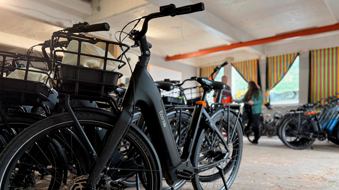 Bilden visar en lokal med flera parkerade elcyklar som det står Ecoride på. I bakgrunden står två personer.