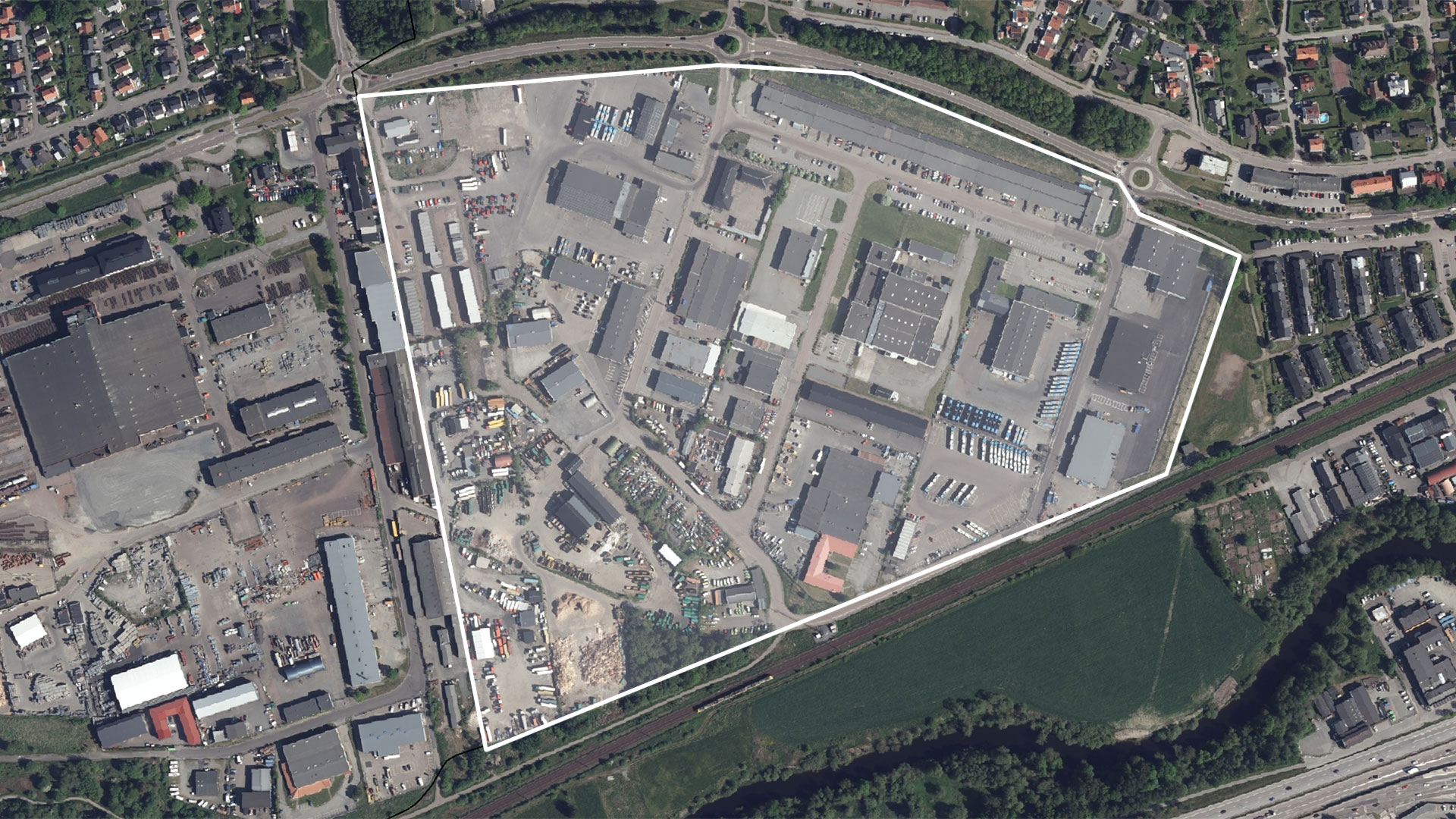 Ortofoto över stadsbebyggelse och industriområde som är markerat med vit linjemarkering och  vit färg med låg opacitet.