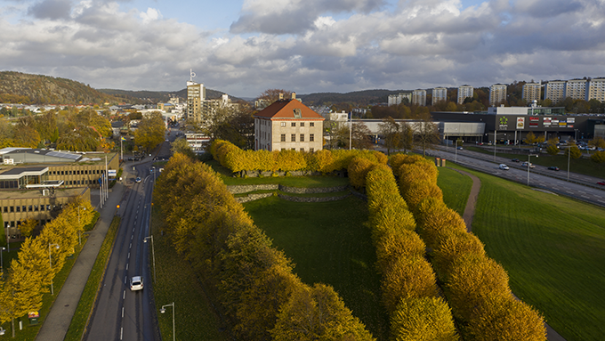 Bild ovanfrån över centrala Partille. Främst i bild syns en tegelbyggnad i tre våningar som är Partille herrgård samt ett envåningshus i brun sten som är Partille kommhus. Bakom dessa ett centrumområde med ett nybyggt 12-våningshus centralt i bilden. 