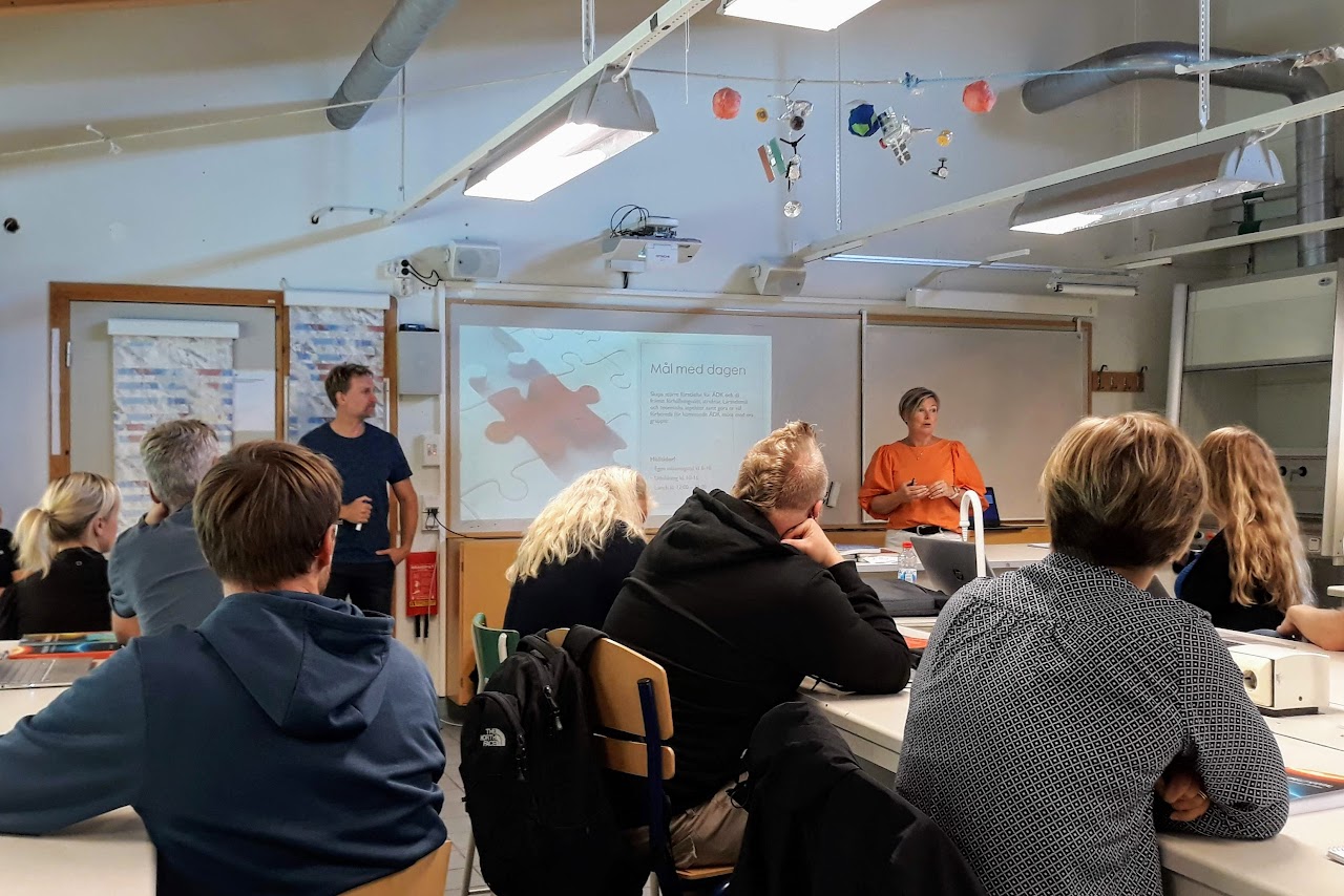 Bilden visar Maria Bergqvist och Henrik Hansson längst fram  i ett klassrum där en projicerad bild visas på Whiteboarden, vid bänkarna sitter flera personer och lyssnar. 