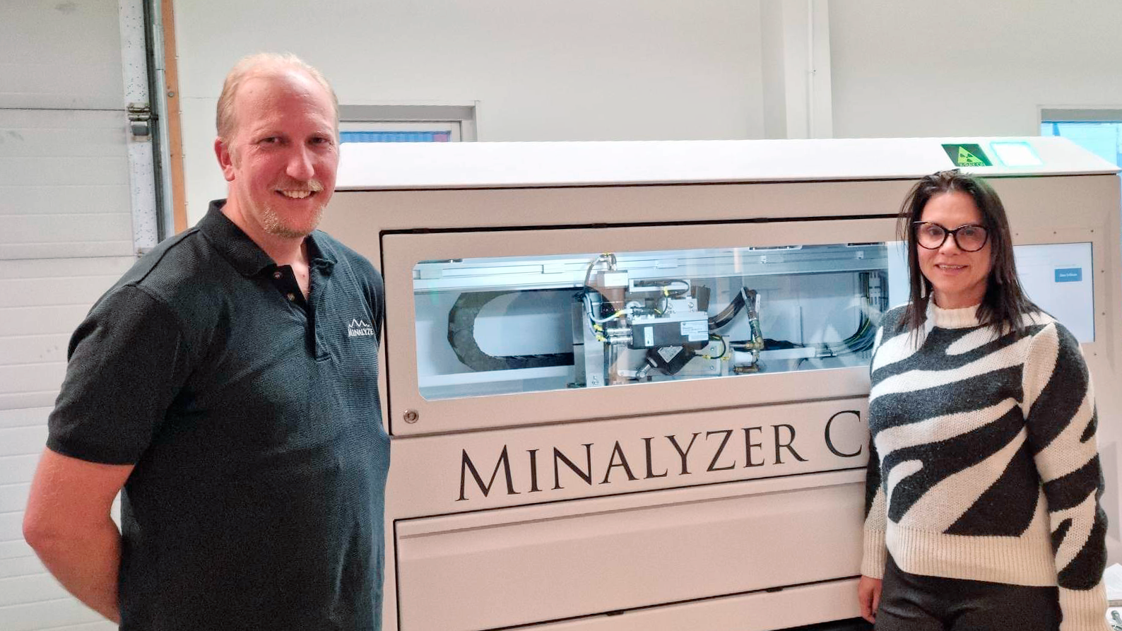 Två personer står framför en maskin i en industriliknande lokal.