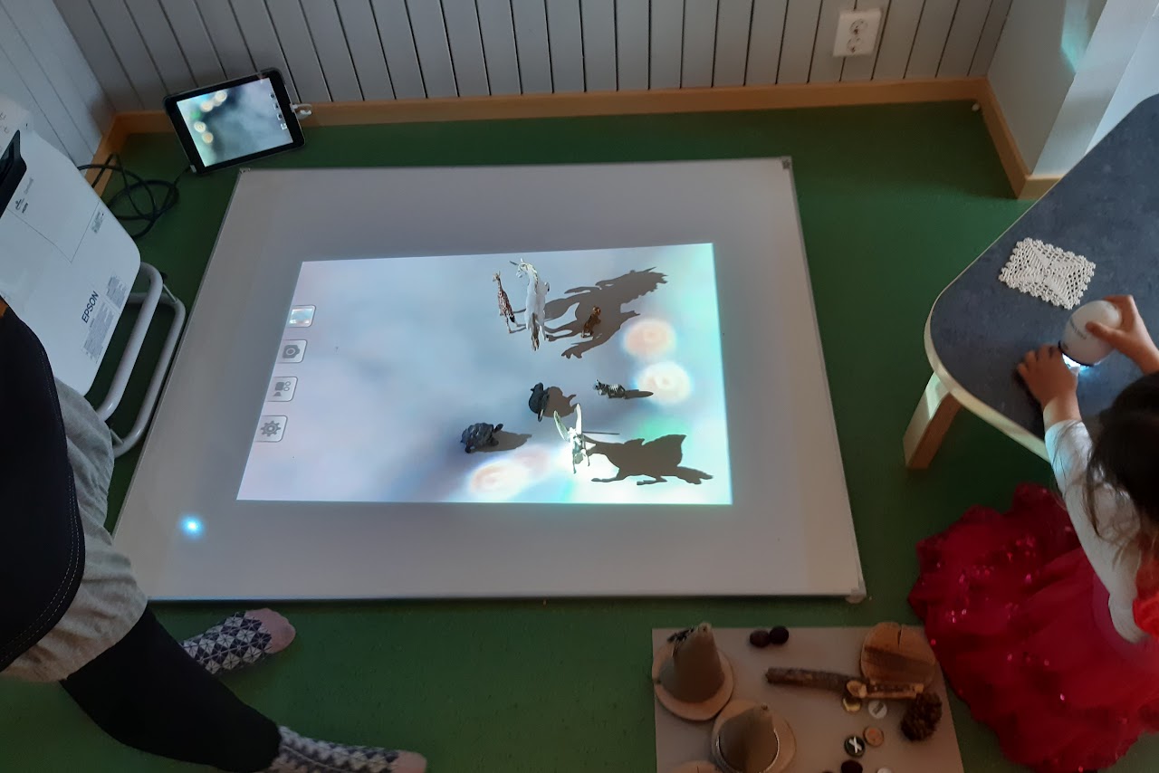 Bilden visar en Whiteboard på ett golv, på den projiceras ljus med färgade prickar i och på Whiteboarden står också sju stycken leksaksdjur. 