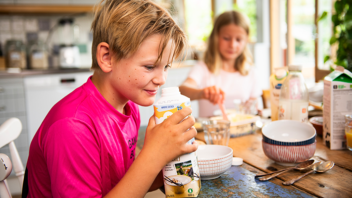 Bild på en pojke i 10-årsåldern som luktar på innehållet i ett mjölkpaket.