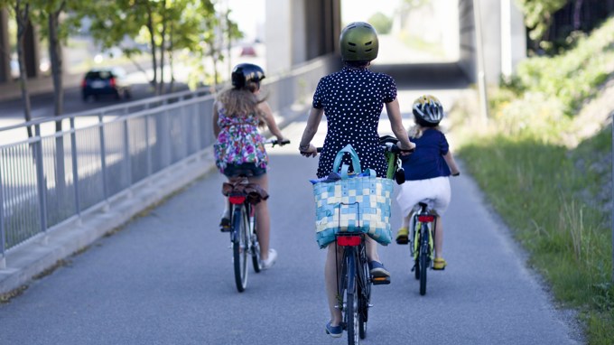 Bilden visar en vuxen person och två barn som cyklar på en väg som är avskild från biltrafik.