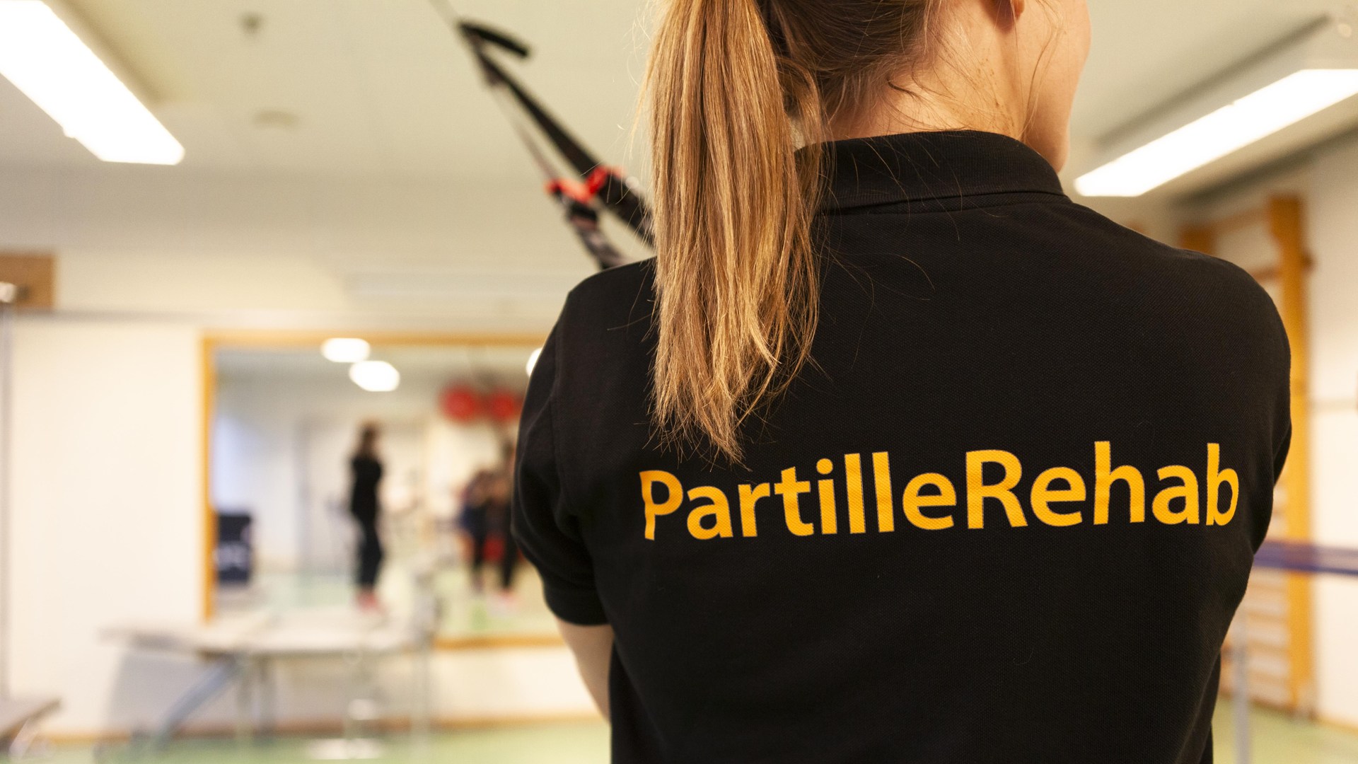 Person står med ryggen mot kameran. perosnen har en svart t-shirt där det står PartilleRehab.