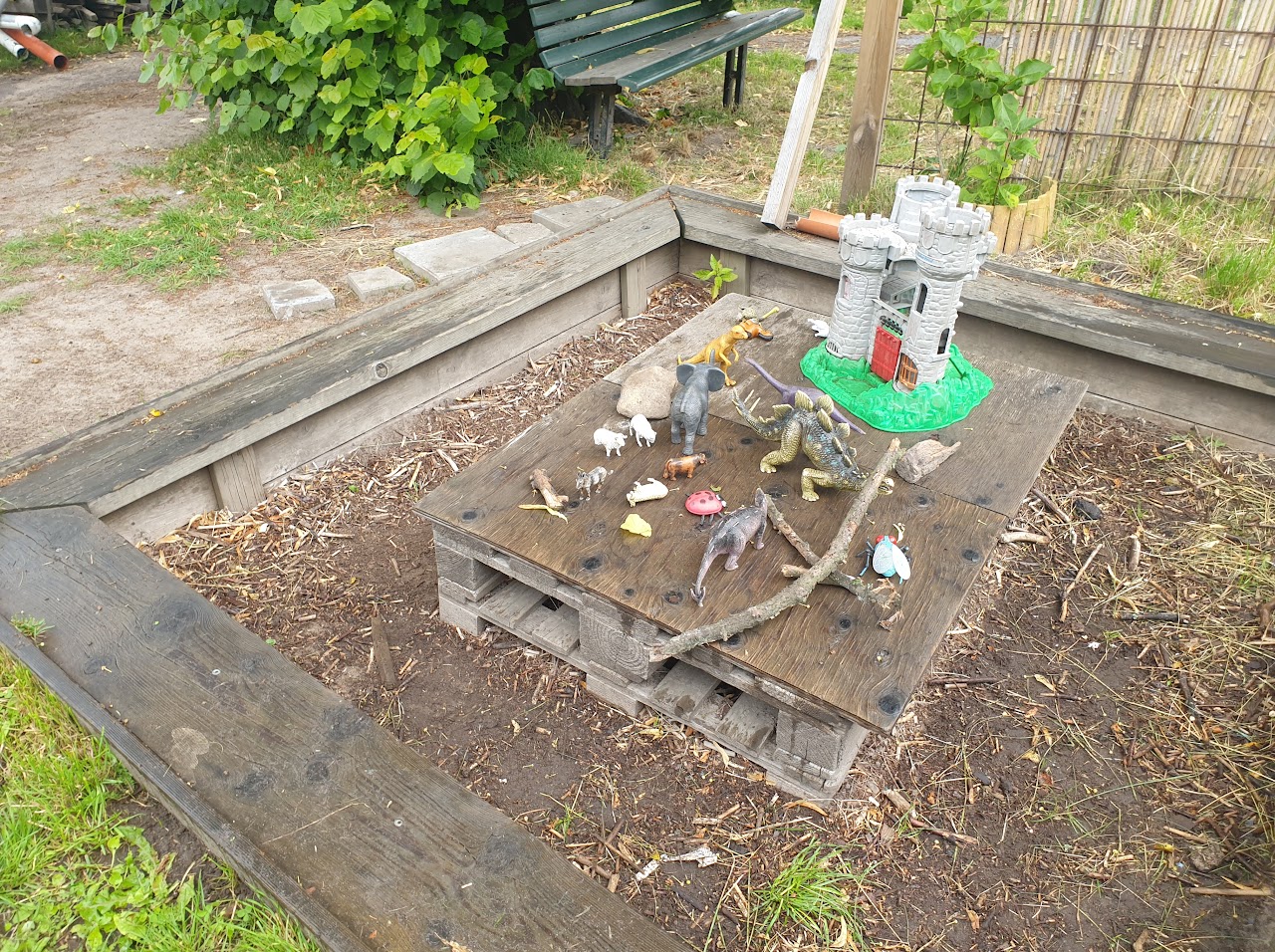 Bilden visar två stycken EU pallar som ligger på varandra, på den översta ligger en plywood skiva och på den står flera leksaksdjur i plast samt en leksaksborg. 