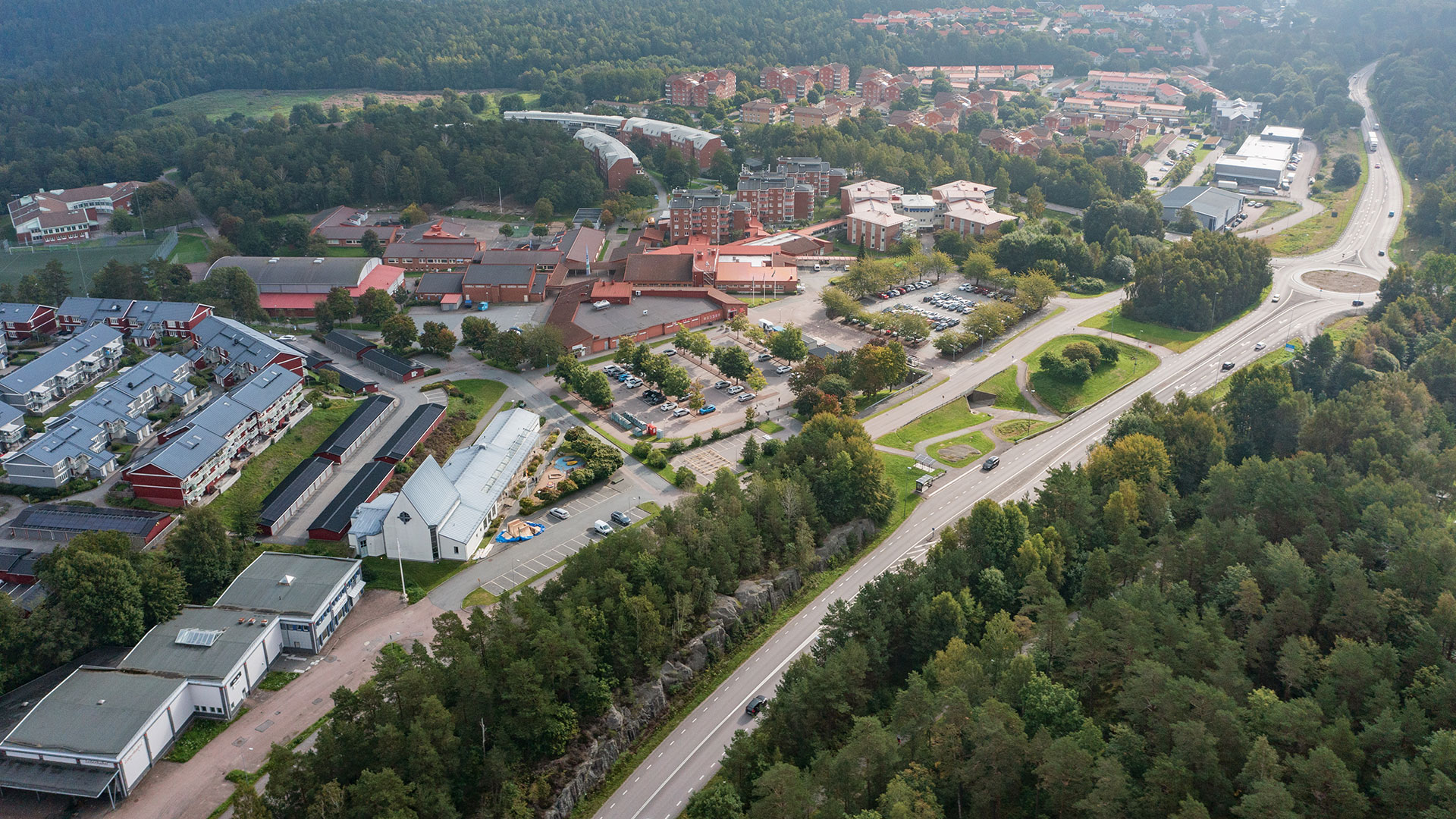 Bilden är ett drönarfoto över stadsbebyggelse och en större väg för motortrafik.
