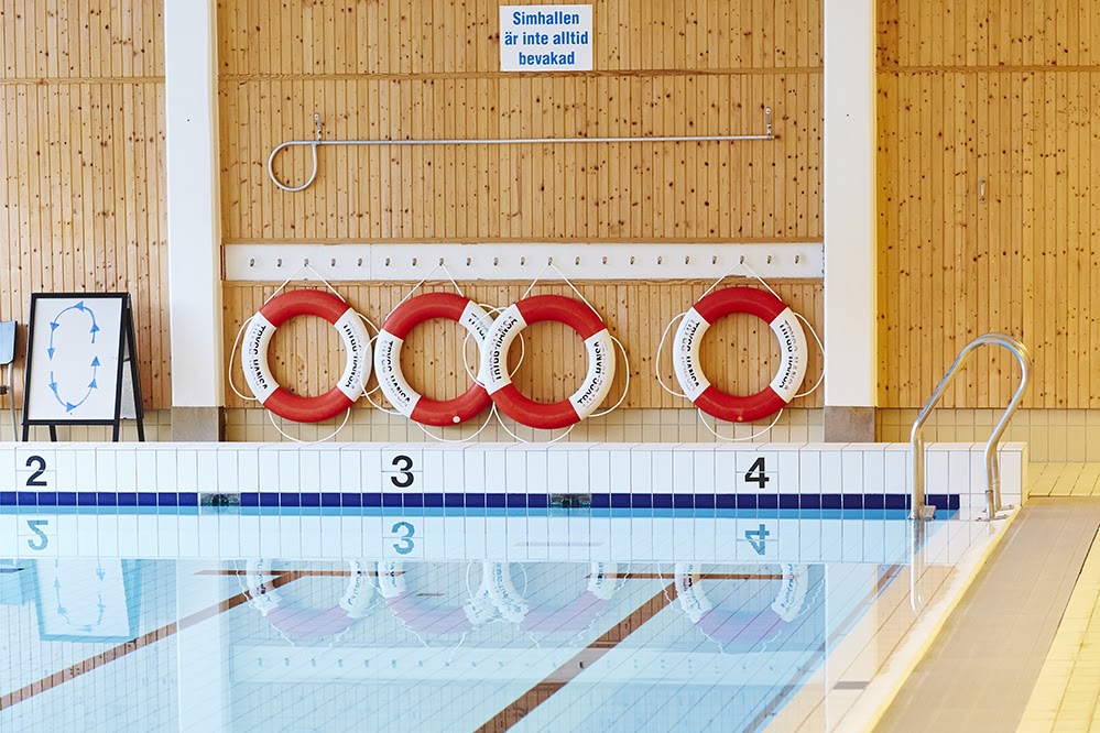 Bild på en simbassäng med numrerade längder i en simhall. Ovanför bassängen hänger fyra stycken livbojar på en vägg med furupanel. 