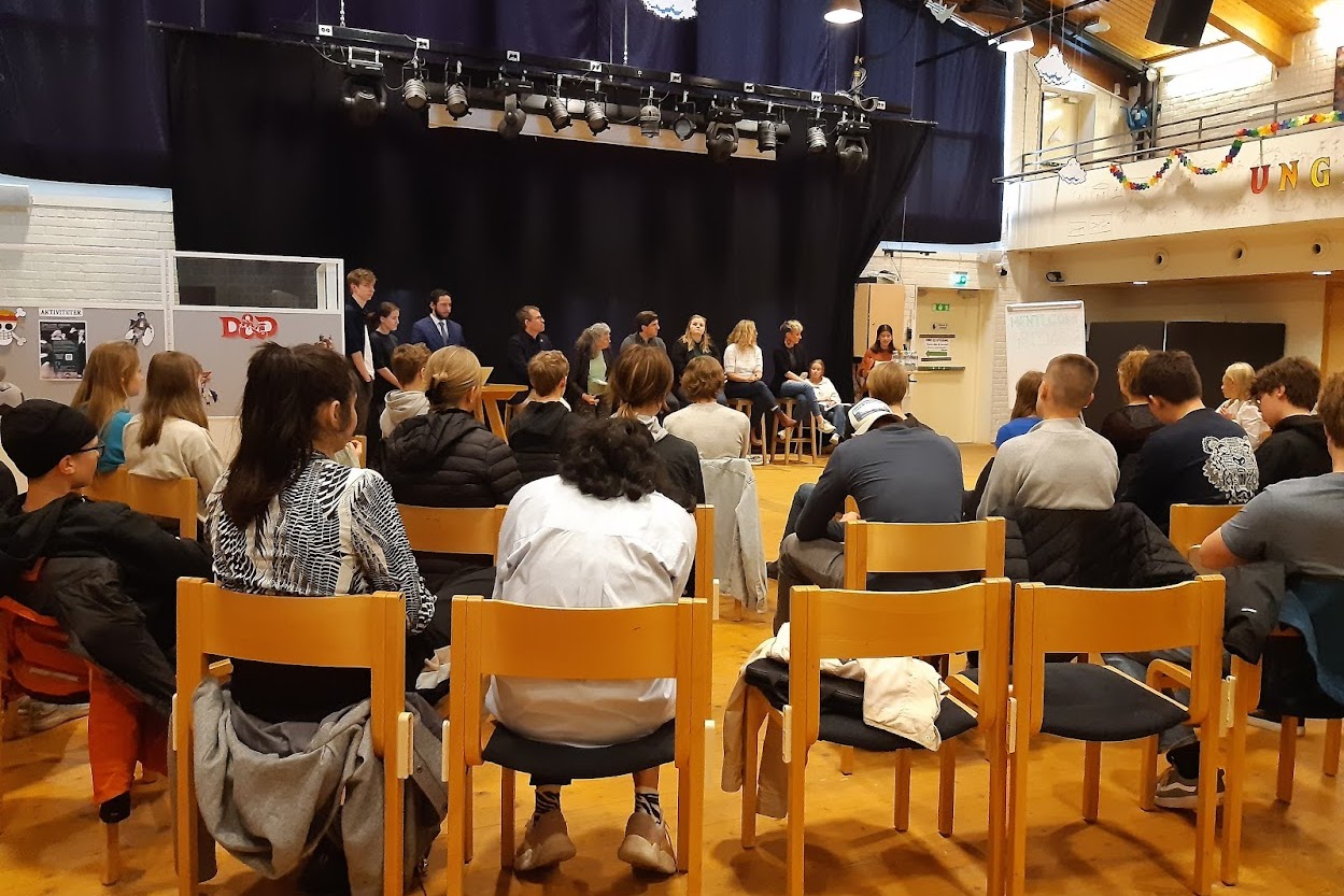 Bild på politiker samt ungdomar som sitter i en stor sal. 