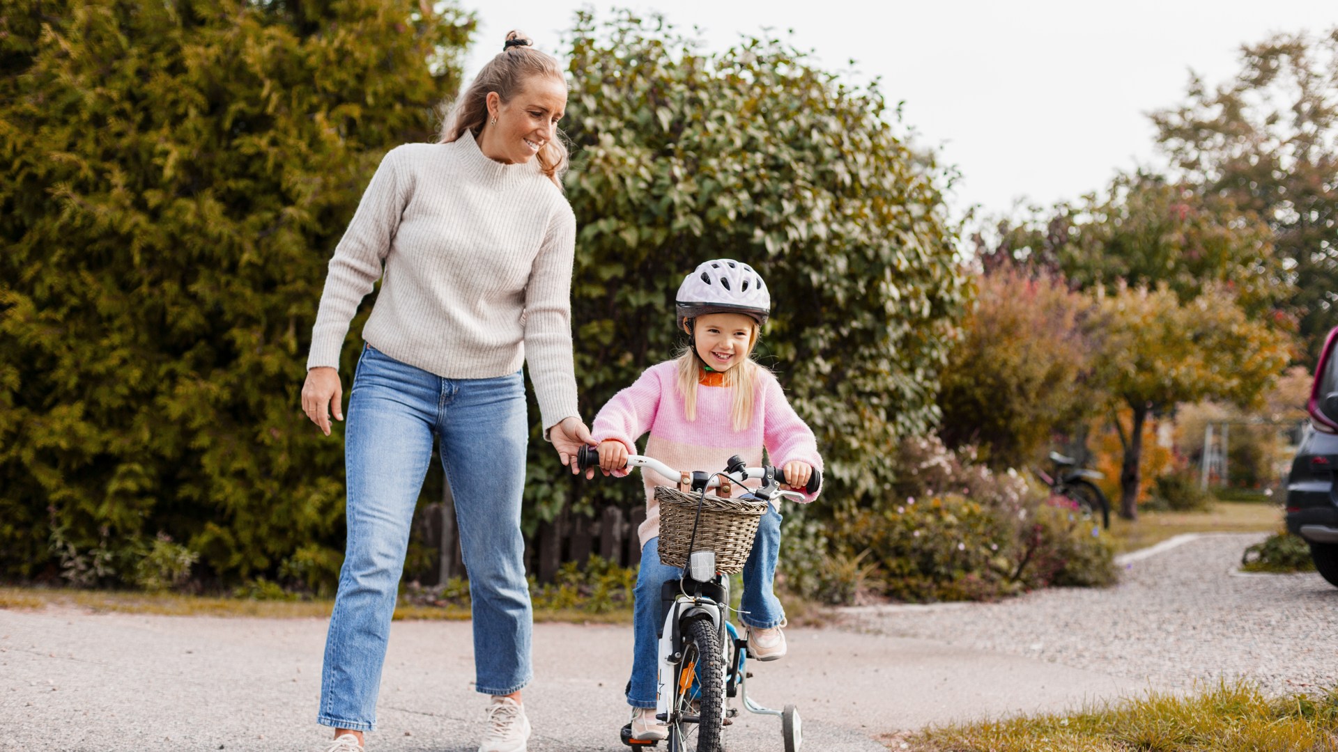 Flicka cyklar med mamma i bakgrunden