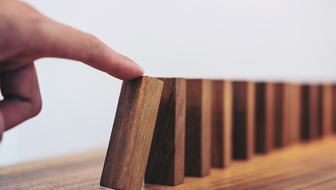 Bild på finger som knuffar till en dominobricka.