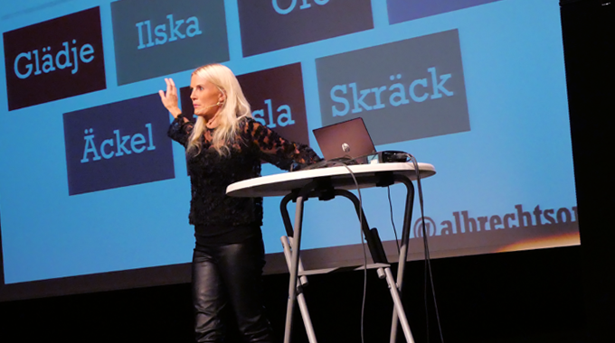 Therese Albrechtson står på scenen i Partille Gymnasiums aula. Vid sidan står ett bord med en dator på. 