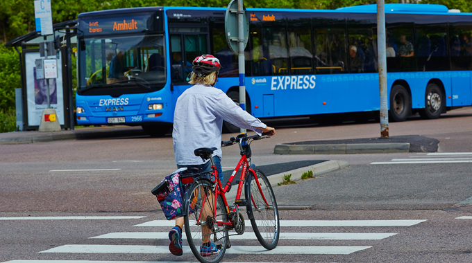 Bild som visar en blå buss. Framför bussen leder en person en cykel över ett övergångsställ. 