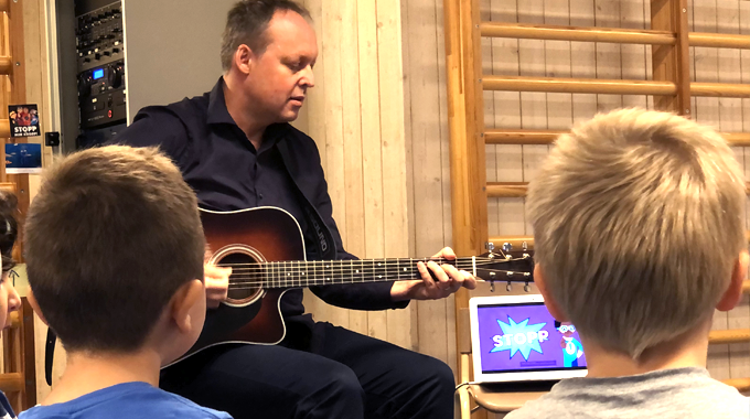 Bild som visar en musiklärare som spelar gitarr och sjunger tillsammans med förskolebarn. 