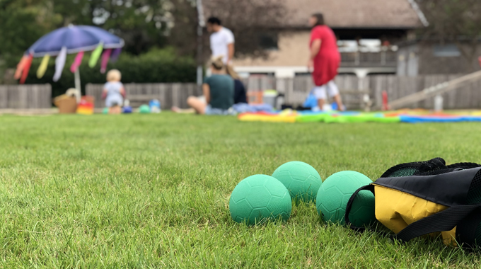 Bild som visar ett bocciaspel. I bakgrunden syns människor som sitter på en grön gräsmatta på filtar. 