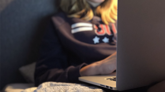 Bild av en ung person som sitter med en dator hemma i sängen. 