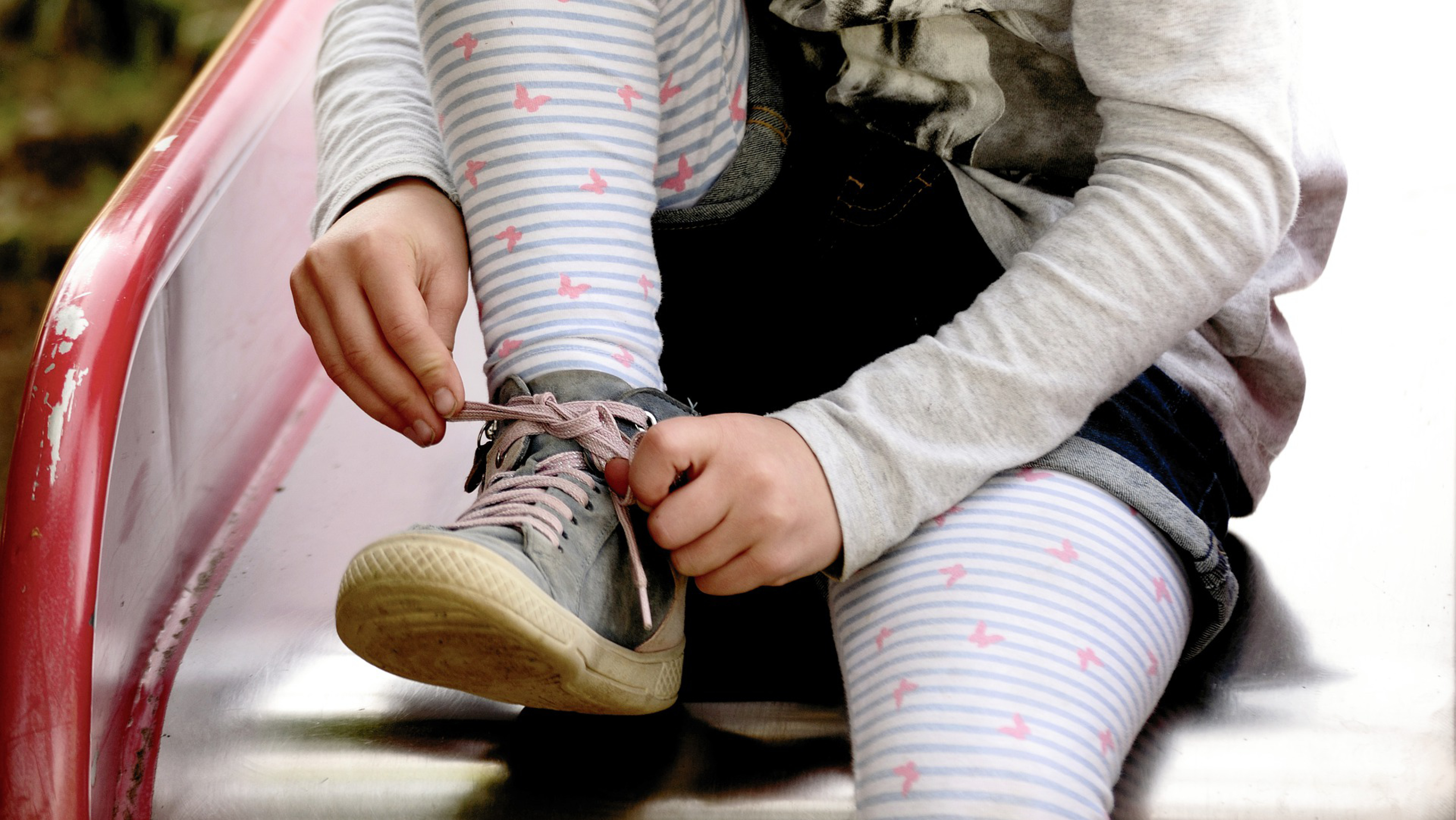 Bilden visar ett barn som sitter på en rutschkana och knyter sin ena gymnastiksko.