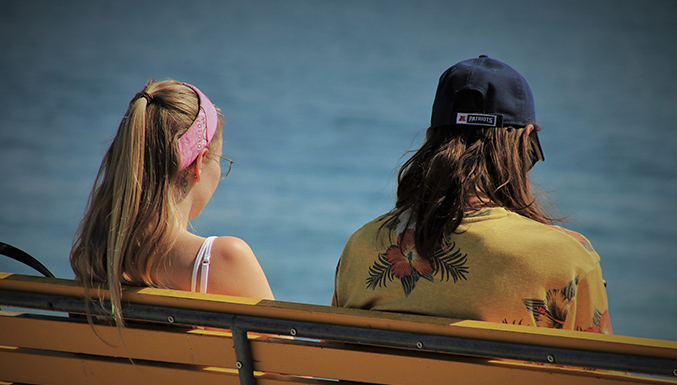 Bilden visar en kvinna och en man som sitter på en bänk och blickar ut över vatten.