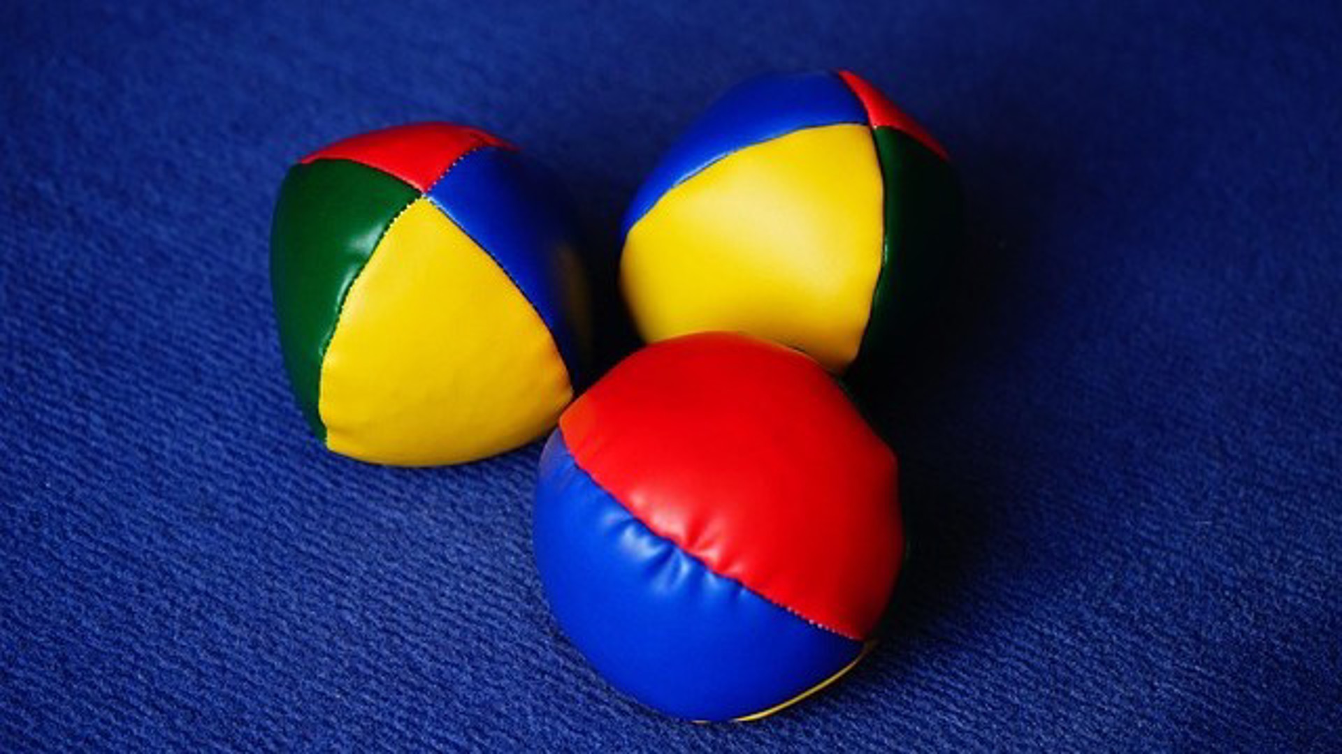 Tre färgglada jongleringsbollar mot en blå bakgrund.