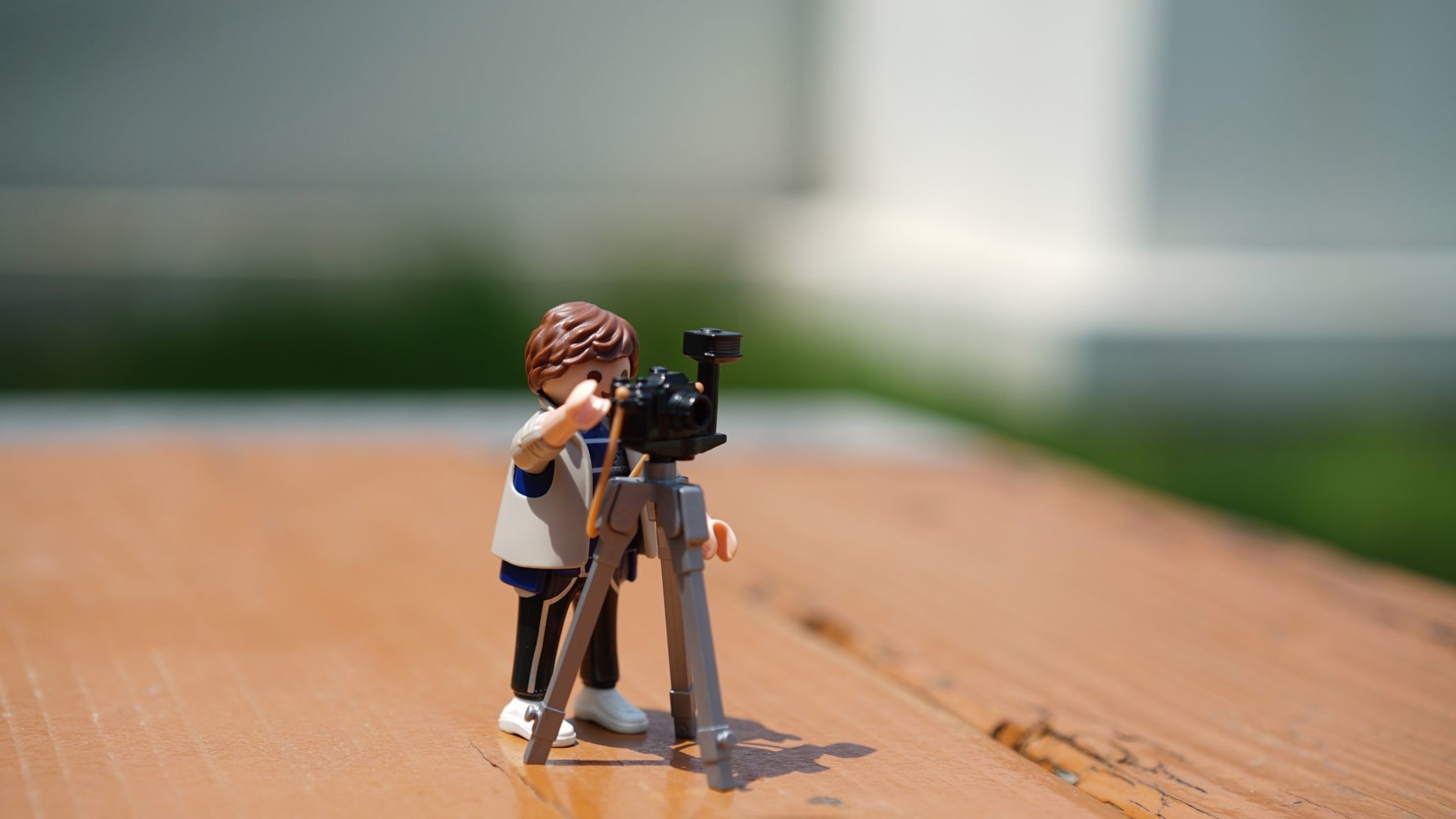 En playmobilgubbe har riggat en filmkamera på ett stativ och står och tittar genom kameran.