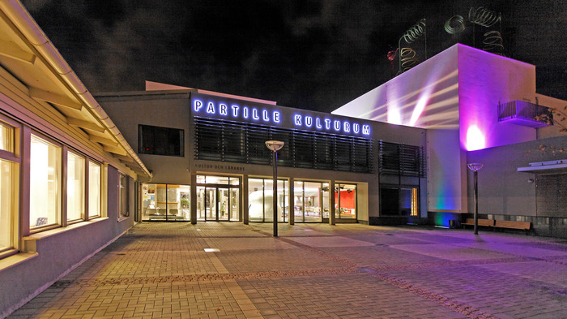 Bild på entrén till Partille Kulturum upplyst på kvällstid.