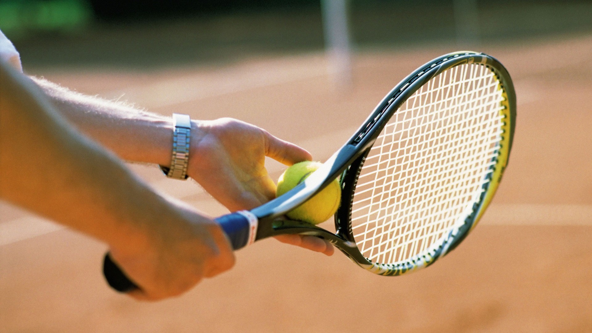 Bild på en händer som håller en tennisboll och ett tennisracket.