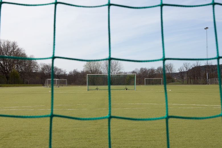 En bild på en fotbollsplan, tagen genom nätet på ett fotbollsmål. 